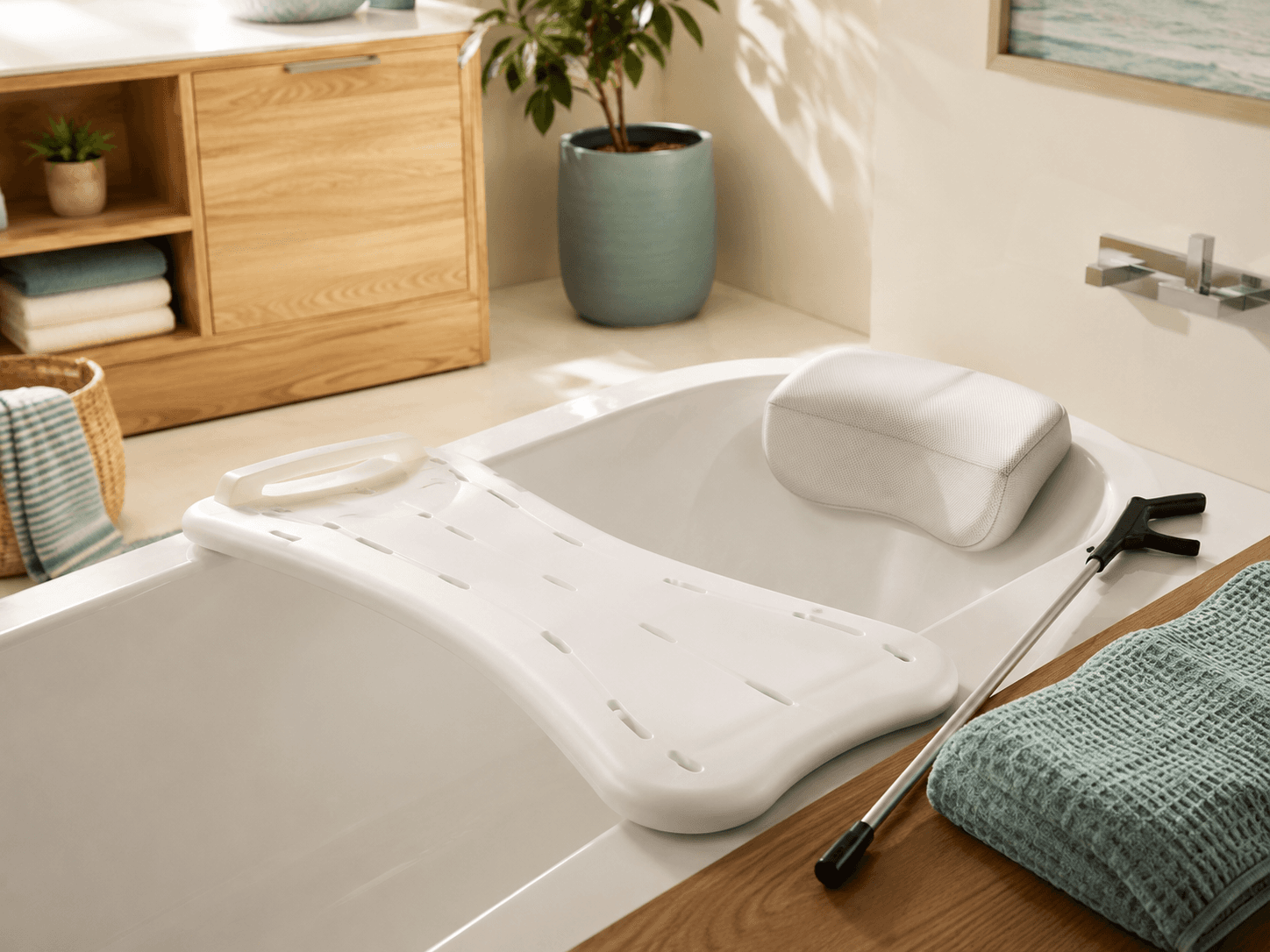 A bath board resting across a bathtub with a neck pillow and a reacher grabber alongside